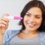 A smiling woman holds up a pregnancy test, expressing joy and anticipation—symbolizing the beginning of a fertility journey and the emotional significance of early pregnancy discovery.