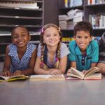 Three smiling children sit close together in a classroom or learning space, representing joy, diversity, and the importance of early childhood development and inclusive care.