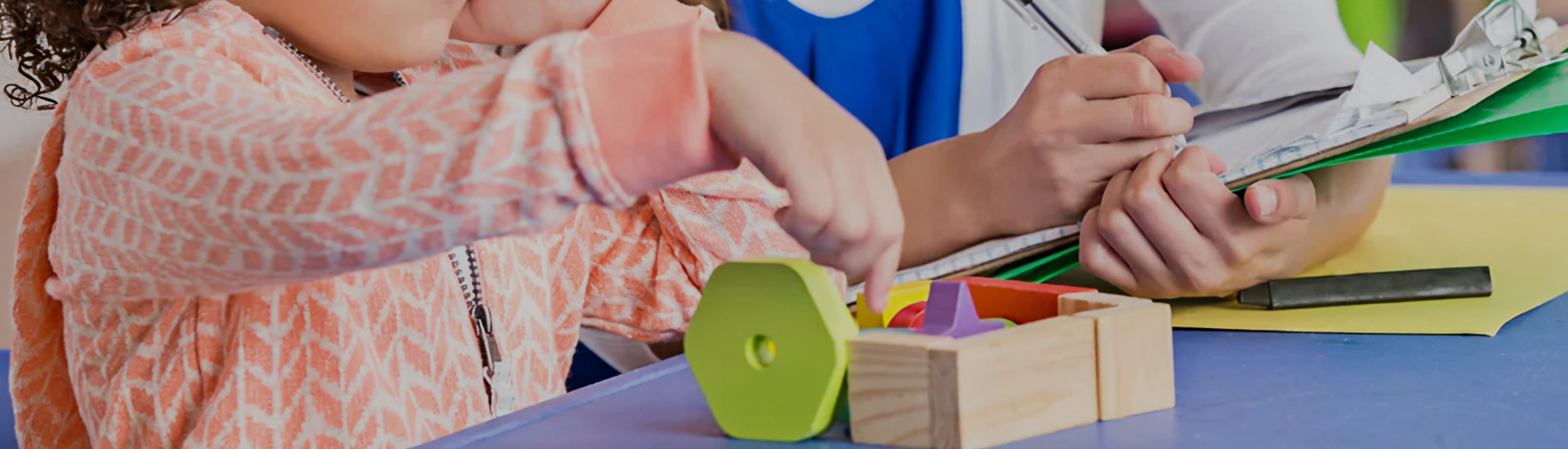 A child engages in a hands-on activity with colorful shapes while a clinician takes notes nearby—illustrating developmental assessment, occupational therapy, or early intervention in a supportive setting.