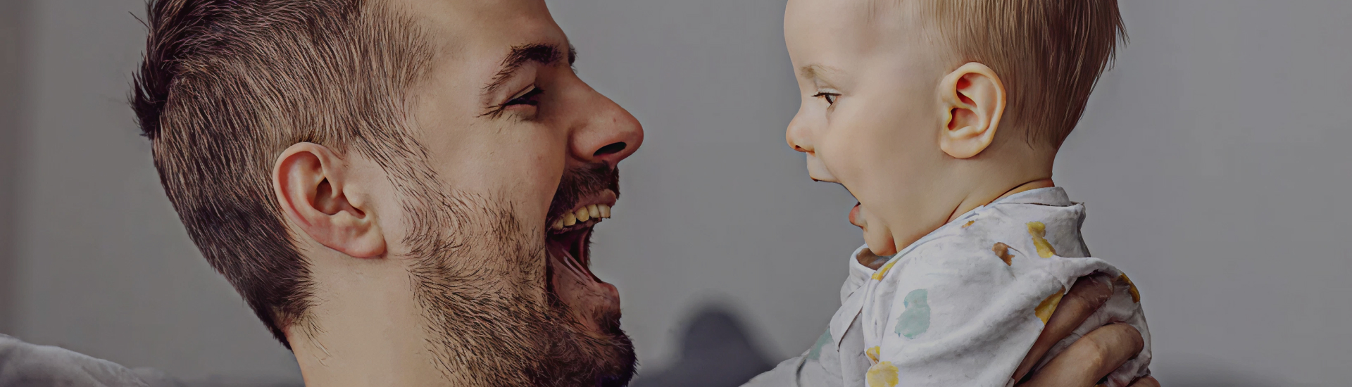 A smiling father joyfully lifts his baby in the air, their faces close together and full of laughter—capturing the warmth of early bonding and the joy of parenthood.
