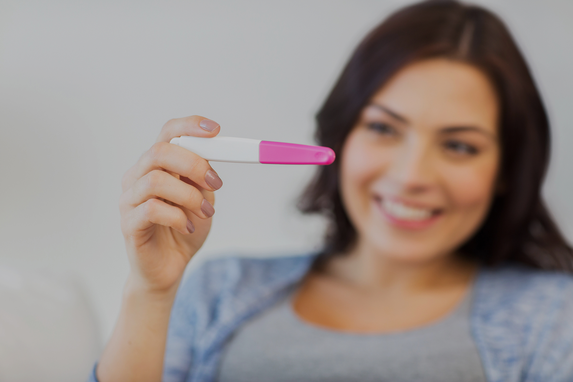 A smiling woman holds up a pregnancy test, expressing joy and anticipation—symbolizing the beginning of a fertility journey and the emotional significance of early pregnancy discovery.