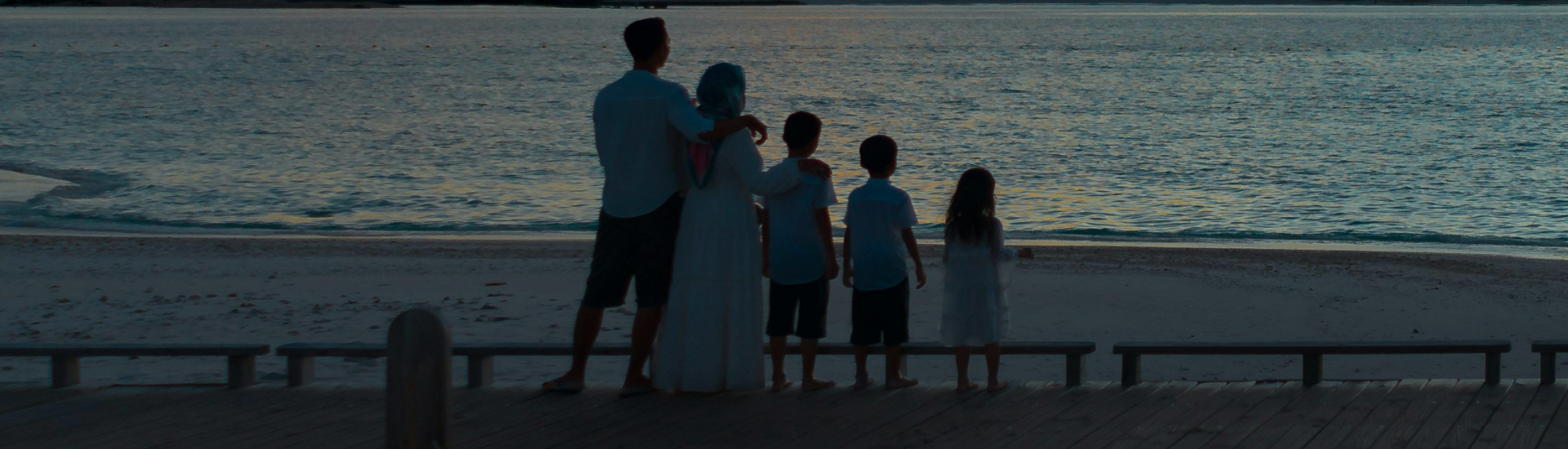 A family stands together at the edge of a beach at sunset, gazing out at the ocean—symbolizing unity, reflection, and the peaceful strength of family connection.
