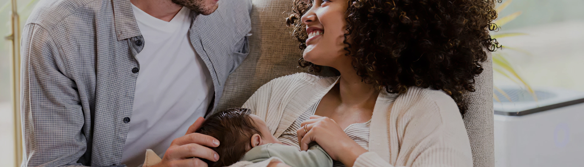 A smiling couple sits together as the mother breastfeeds their baby, sharing a joyful moment of connection, support, and early parenthood.