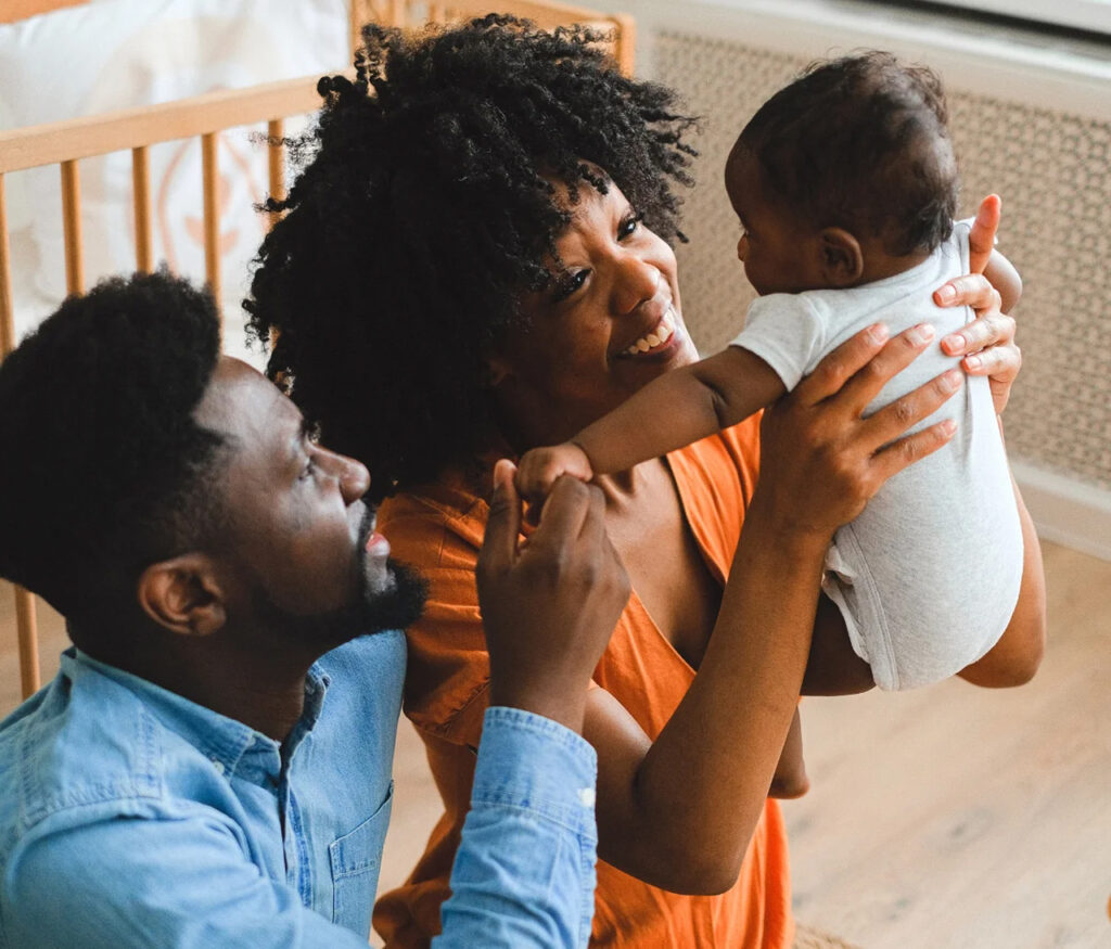 wo joyful parents smile as they lovingly hold up their baby in a cozy nursery, capturing the warmth, connection, and tender bonding of early parenthood.
