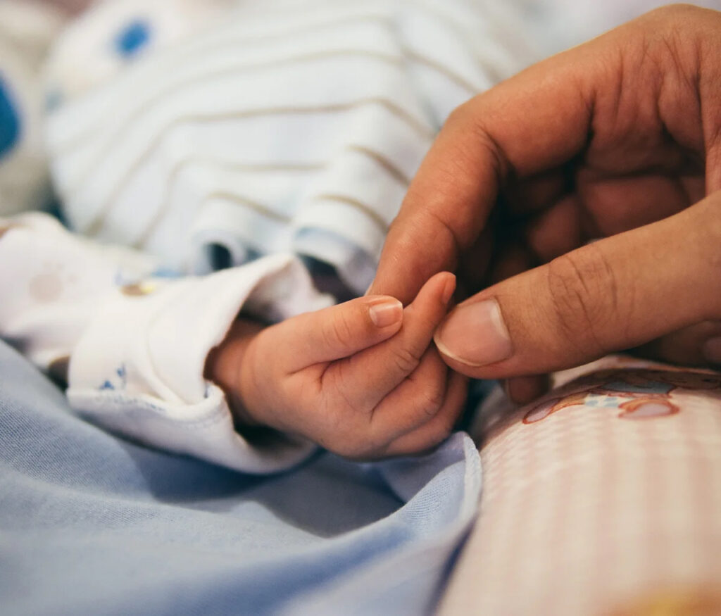 A close-up of a newborn gently grasping an adult’s finger, symbolizing the tenderness, trust, and deep connection between parent and baby during the early stages of life.