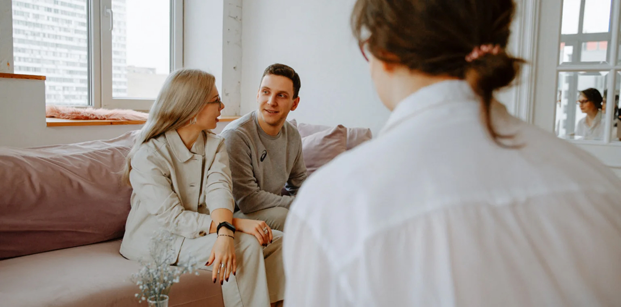 A couple sits on a couch engaged in conversation with a therapist.