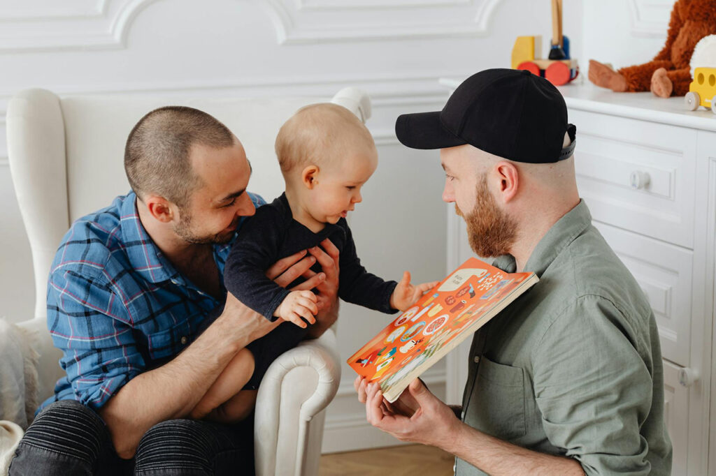 Two dads with their child, reading a book symbolizing family togetherness