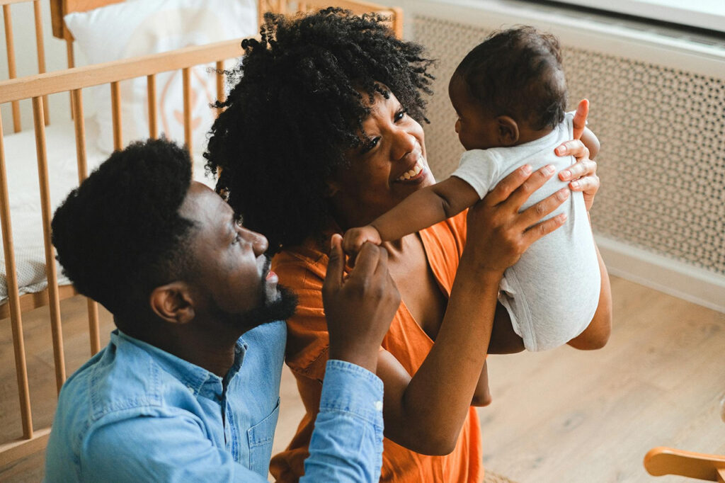 Two smiling parents joyfully engage with their baby in a nursery, capturing a moment of love, connection, and the shared joy of early parenthood.